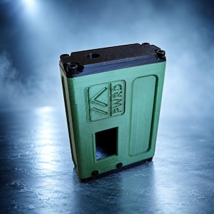 Peut inclure: Un boîtier d'appareil rectangulaire vert olive avec une plaque supérieure noire fixée par quatre vis. L'avant présente une ouverture rectangulaire encastrée et un logo carré en relief contenant le texte PWRD avec deux flèches vers le haut.