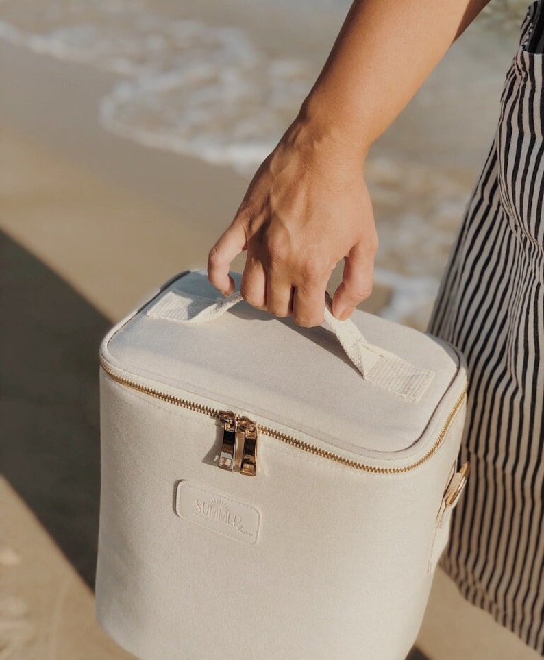 May include: A white canvas cooler bag with a gold zipper and handle. The bag has the word "SUMMCO" printed on the front.