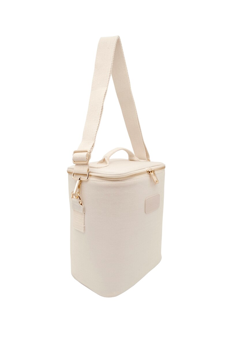 May include: A white canvas lunch bag with a gold zipper and a gold strap. The bag has a rectangular shape and a small patch on the front.