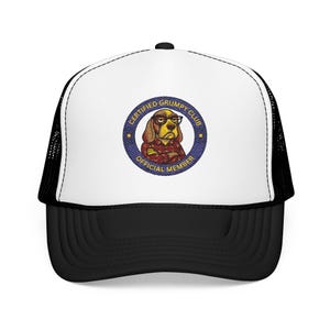 May include: A black and white trucker cap with a white front panel. The panel displays a circular patch with the text "CERTIFIED GRUMPY CLUB OFFICIAL MEMBER" around a cartoon dog wearing glasses and a red plaid shirt.