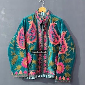 Puede incluir: Chaqueta de terciopelo turquesa con intrincados bordados florales en rosa, naranja y dorado. La chaqueta tiene un cuello alto y un forro a rayas. El texto "Fezanhandicraft" es visible.