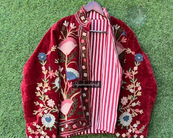 Könnte beinhalten: Eine rote Samtjacke mit Blumenstickerei. Die Jacke hat einen Stehkragen und ein gestreiftes Futter. Die Stickerei ist in den Farben Rosa, Blau und Grün gehalten.
