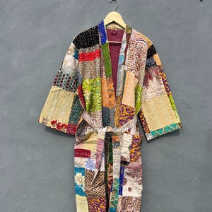 Könnte beinhalten: Ein Patchwork-Bademantel mit einer Vielzahl von bunten Stoffquadraten. Der Bademantel hat lange Ärmel und einen passenden Gürtel. Der Bademantel hängt an einem Holzbügel vor einem grauen Hintergrund. Der Bademantel ist eine Mischung aus Mustern und Farben.