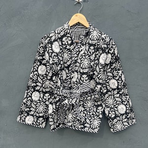 Könnte beinhalten: Schwarze Jacke mit weißem Blumendruck und einem Bindegürtel. Die Jacke hat einen V-Ausschnitt und lange Ärmel.