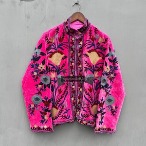Puede incluir: Una chaqueta de terciopelo rosa con intrincados bordados florales en tonos azules, rojos y dorados. La chaqueta tiene un cuello mandar&iacute;n y cierre de botones. El texto "Fezanhandicraft" es visible en la parte delantera de la chaqueta.