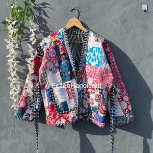 May include: A colorful patchwork quilted jacket with a black and white striped lining. The jacket has a tie closure and long sleeves.