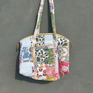 Peut inclure: Un sac cabas en patchwork avec une variété de motifs floraux et géométriques dans des tons de bleu, vert, rose, jaune et blanc. Le sac a deux longues anses et une fermeture à glissière.