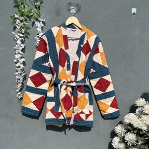 Puede incluir: Una chaqueta acolchada con un patrón geométrico en tonos de rojo, azul, amarillo y blanco. La chaqueta tiene un cinturón de atar y está hecha de algodón. "Fezan Handicraft" está impreso en el cinturón.