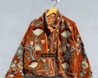 May include: A brown velvet jacket with intricate floral embroidery in shades of blue, white, and orange. The jacket has a button closure and long sleeves.