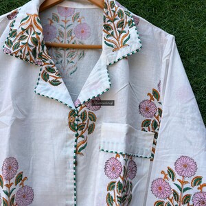 May include: White cotton pajama top with a green and orange floral print. The top has a button-up front, a collar, and a pocket on the left side.