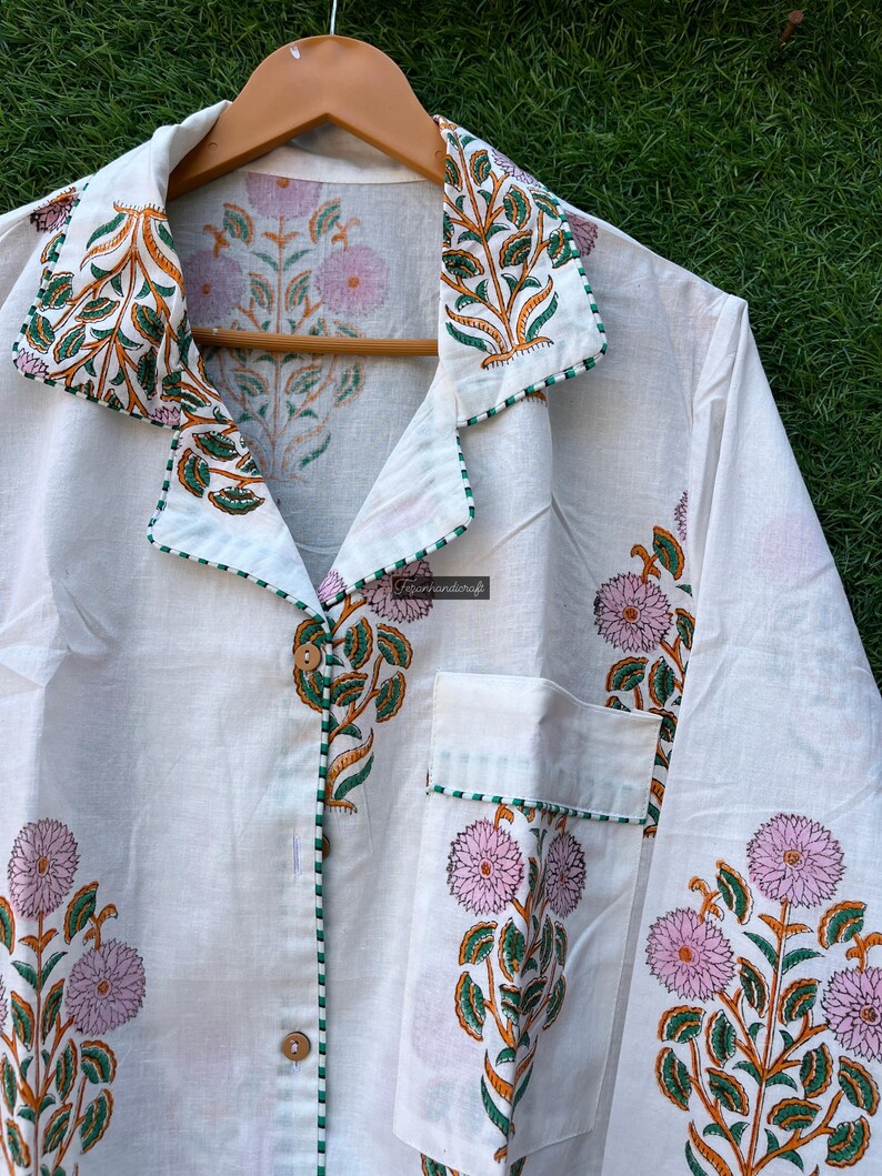 May include: White cotton pajama top with a green and orange floral print. The top has a button-up front, a collar, and a pocket on the left side.