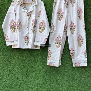 May include: White cotton pajama set with a floral print in shades of pink, green, and orange. The set includes a long-sleeved shirt with a button-up front and matching pants.
