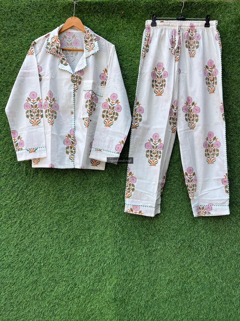 May include: White cotton pajama set with a floral print in shades of pink, green, and orange. The set includes a long-sleeved shirt with a button-up front and matching pants.