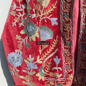 May include: A red velvet jacket with intricate floral embroidery in shades of blue, green, gold, and pink. The jacket has a traditional design and is a beautiful example of hand-crafted artistry.