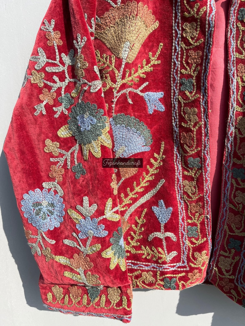 May include: A red velvet jacket with intricate floral embroidery in shades of blue, green, gold, and pink. The jacket has a traditional design and is a beautiful example of hand-crafted artistry.