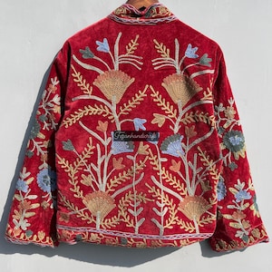 May include: Red velvet jacket with intricate floral embroidery in shades of gold, blue, and green. The jacket has a mandarin collar and long sleeves.