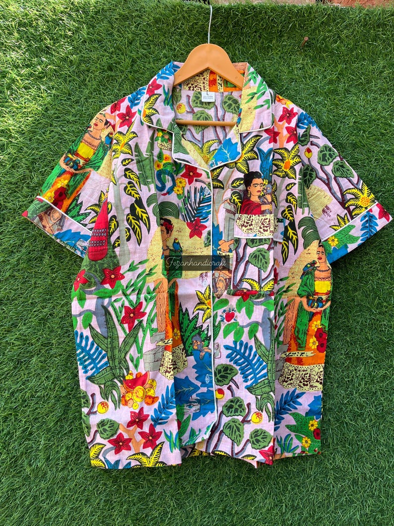 Puede incluir: Una camisa rosa de botones con estampado floral colorido con im&aacute;genes de Frida Kahlo. La camisa tiene un cuello blanco y un ribete blanco alrededor de las mangas y el cuello.