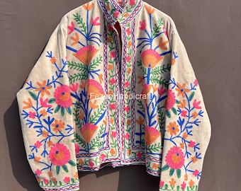 Può includere: Giacca beige con vivaci ricami floreali in rosa, arancione e blu. La giacca presenta un collo alto e una chiusura con bottoni. Il design floreale è dettagliato e copre la parte anteriore e le maniche.
