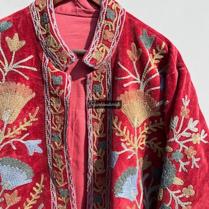 May include: A red velvet jacket with intricate floral embroidery in shades of blue, green, and gold. The jacket has a mandarin collar and a button closure.