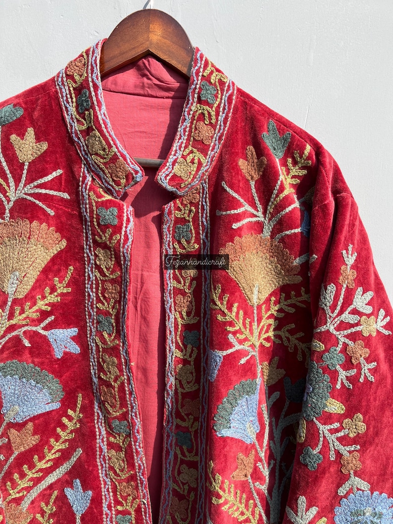 May include: A red velvet jacket with intricate floral embroidery in shades of blue, green, and gold. The jacket has a mandarin collar and a button closure.
