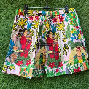 Puede incluir: Un par de pantalones cortos de algod&oacute;n rosa y blanco con un estampado floral colorido que presenta una imagen repetida de una mujer con una flor en el pelo. El estampado tambi&eacute;n incluye loros, flores y hojas.