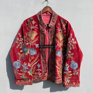 May include: A red velvet jacket with intricate floral embroidery in shades of blue, green, and gold. The jacket has a mandarin collar and a front closure.