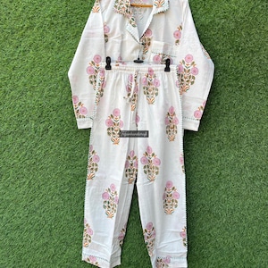 May include: White cotton pajama set with a floral print in pink, green, and orange. The set includes a long-sleeved shirt with a collar and a pair of pants with an elastic waistband.