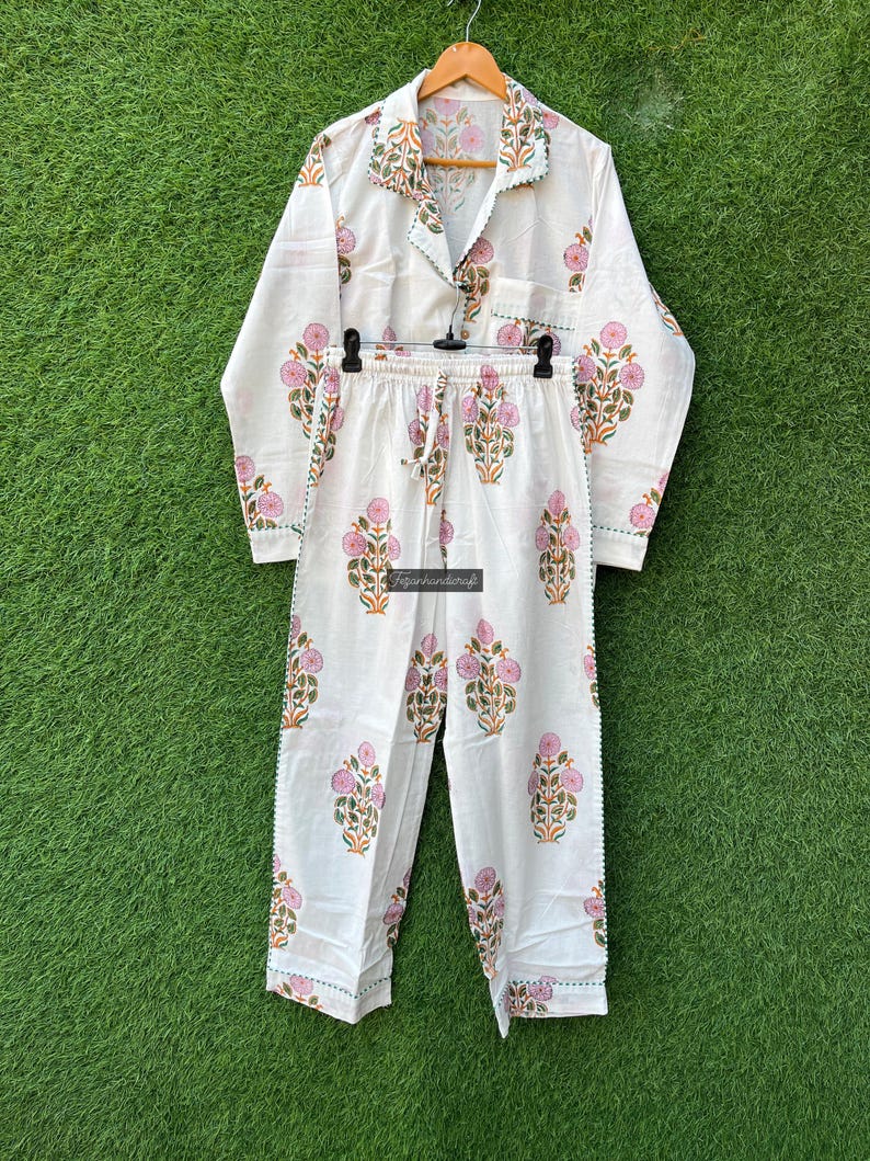 May include: White cotton pajama set with a floral print in pink, green, and orange. The set includes a long-sleeved shirt with a collar and a pair of pants with an elastic waistband.