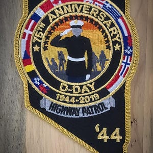May include: Black patch with gold trim, commemorating the 75th Anniversary of D-Day, 1944-2019. Features a saluting soldier, flags, and the words "Highway Patrol" and "'44".