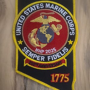 以下が含まれることがあります： アメリカ海兵隊のエンブレムが刺繍されたパッチ。パッチは黒色で、黄色の縁取りがあり、「United States Marine Corps」と「Semper Fidelis」の文字が含まれています。エンブレムには、ワシ、地球、錨のデザインと1775年という年が含まれています。