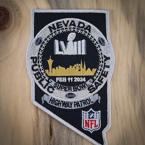 May include: A black and white embroidered patch with the text "Nevada Public Safety Highway Patrol" and a silver Super Bowl LVIII logo. The patch also features a skyline of Las Vegas and the date "Feb 11 2024". The NFL logo is in the lower right corner.