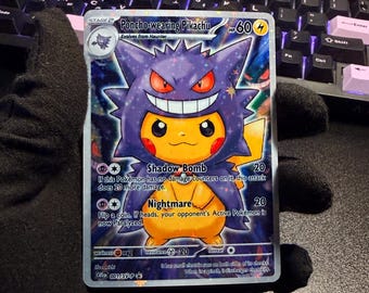 May include: A rectangular trading card featuring a yellow Pikachu character wearing a purple Gengar-themed poncho. The card displays the text Poncho-wearing Pikachu, Shadow Bomb, and Nightmare, with a holographic star pattern across the surface.