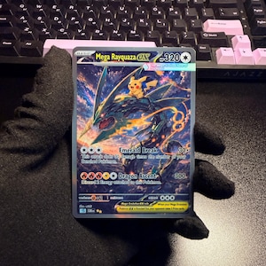 May include: A Mega Rayquaza EX trading card featuring a large, serpentine green dragon with a small yellow Pikachu character on its back. The card displays the text Mega Rayquaza EX, 320 HP, Emerald Break, and Dragon Ascent against a sky background.