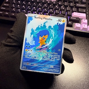May include: A Surfing Pikachu trading card featuring a yellow electric-type character riding a large blue wave. The card displays the name Surfing Pikachu, 80 HP, and the attack Thunder-Riding-The-Wave with descriptive text printed in black.