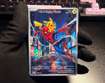 May include: A rectangular trading card titled Web-Swinging Pikachu with 70 HP. The illustration features Spider-Man swinging through a city street with Pikachu on their back. The card includes the attack Electric Web, energy symbols, and text.