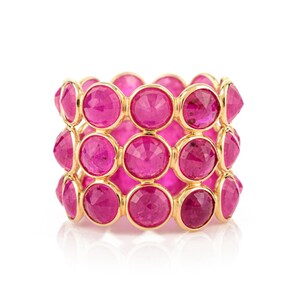 May include: A gold ring featuring three rows of vibrant pink gemstones. The gemstones are round and set closely together, creating a continuous band of color. The ring has a polished gold band.