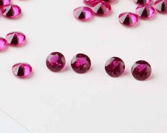May include: A collection of small, round, pink gemstones. The gemstones are scattered on a white surface.