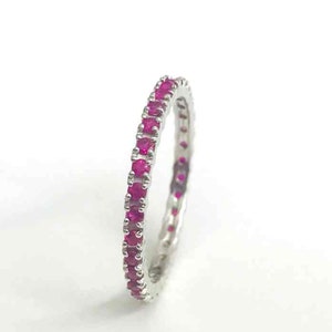 May include: A delicate eternity band ring with a continuous row of small, bright pink ruby stones set in a silver band.