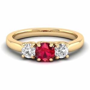 May include: A gold band ring with a red ruby gemstone in the centre and two smaller white diamonds on either side.