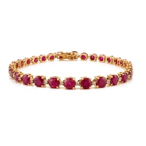 May include: A gold bracelet featuring oval-cut red gemstones. The bracelet is secured with a gold clasp and has small, clear accent stones between each ruby. The gemstones are set in a gold band.