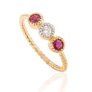 May include: A gold ring with three gemstones. The ring has a beaded band and three circular settings. The settings hold a ruby, a diamond, and another ruby. The gemstones are set in a gold bezel.