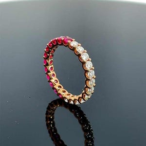 Pode incluir: Um anel de banda de ouro com uma meia volta de pedras de rubi vermelho e uma meia volta de diamantes transparentes.