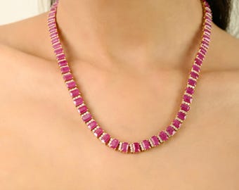 May include: A gold-toned necklace featuring a series of rectangular, vibrant pink gemstones. The gemstones are set closely together, creating a continuous line around the neck. The necklace is a statement piece, likely for special occasions.