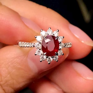 May include: A silver ring featuring a large red ruby gemstone encircled by smaller diamonds. The ring is set in a floral design.