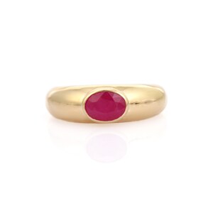 Op de afbeelding: Een gouden ring met een grote, ovaal geslepen robijn. De ring heeft een gladde, gepolijste band en een bezel-zetting die de levendige rode steen stevig vasthoudt. De ring wordt op een witte achtergrond gepresenteerd.