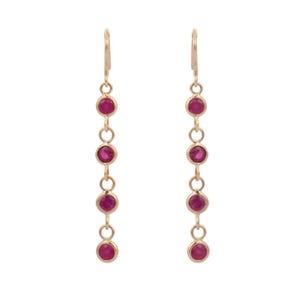 May include: A pair of gold-colored drop earrings, each featuring five round, vibrant red gemstones. The gemstones are evenly spaced and connected by delicate gold links, creating a dangling effect. The earrings have a simple, elegant design.