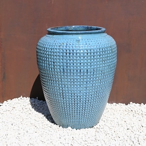May include: A large, blue ceramic planter with a textured, diamond-shaped pattern. The planter is sitting on a bed of white gravel.