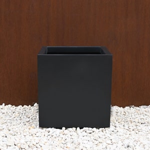 May include: A black square planter made of metal. The planter is sitting on a bed of white gravel.