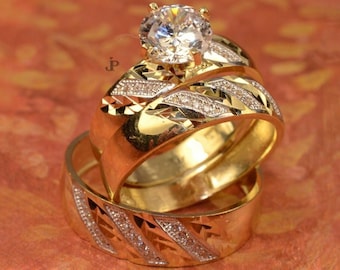 Könnte beinhalten: Ein goldener Ehering-Set mit einem großen, klaren, runden Brillanten in der Mitte und zwei kleineren Ringen mit Diamant-Akzenten.