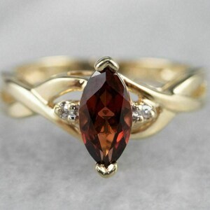 May include: A gold ring with a marquise-shaped garnet gemstone and two smaller diamond accents. The band is twisted and features a delicate design.